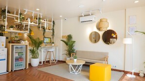 Ein modernes Wohnzimmer mit Fischgrätparkett, einem gelben Hocker, einem grauen Sofa und einem Essbereich mit Holztisch und Stühlen.