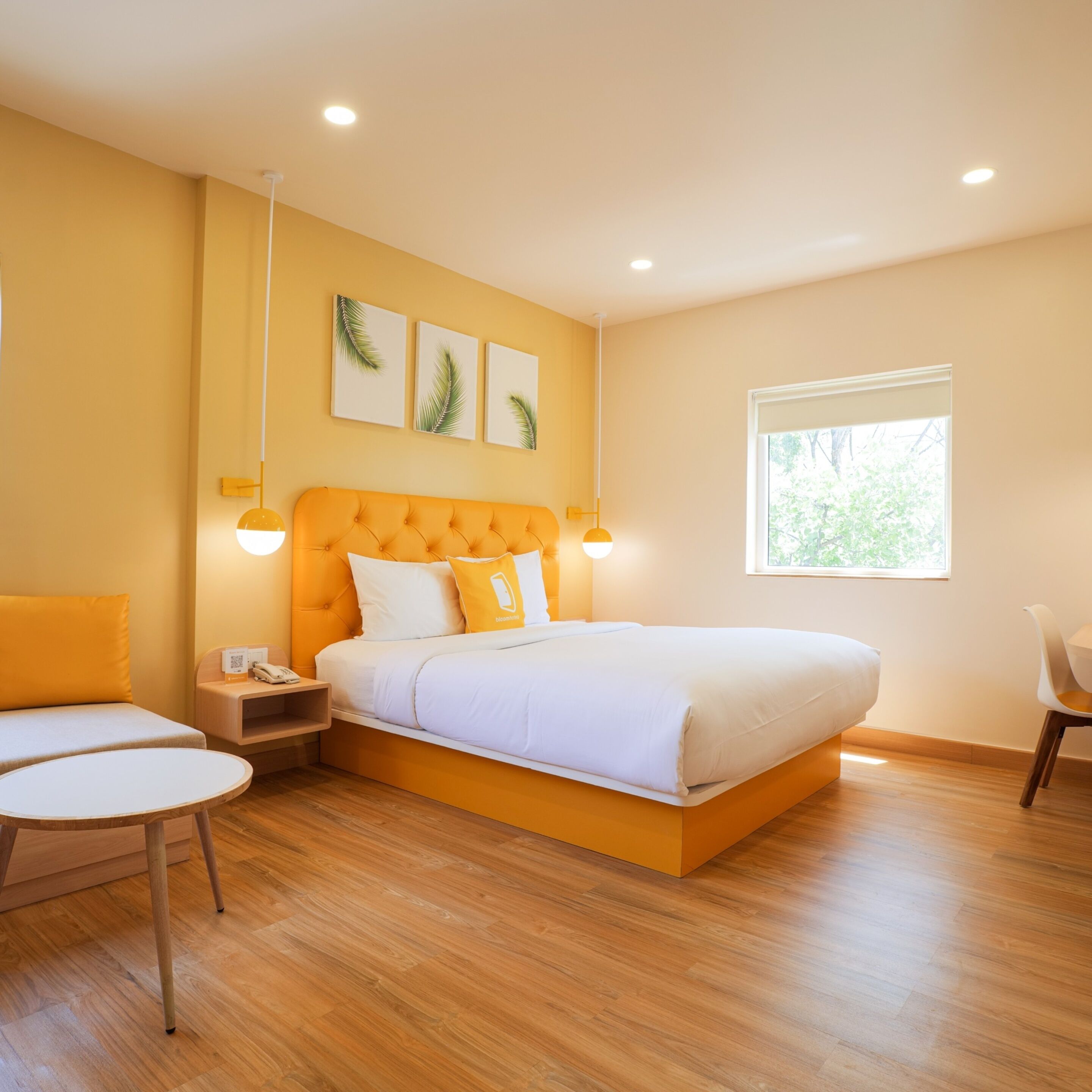 A modern bedroom with a large bed, a bedside table with a phone, a chair, and a window with a view of greenery.
