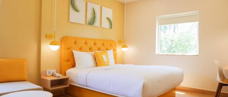 A modern bedroom with a large bed, a bedside table with a phone, a chair, and a window with a view of greenery.