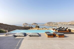 An infinity pool with lounge chairs and a stone wall. - Amazing view Villa Agapi 2' from the beach, by Red Windmill Villas (Mykonos)