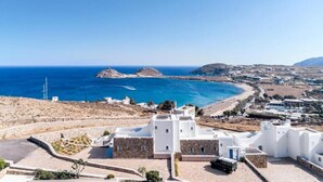 Vista costera con edificios blancos, mar azul cristalino y un paisaje montañoso en la distancia.