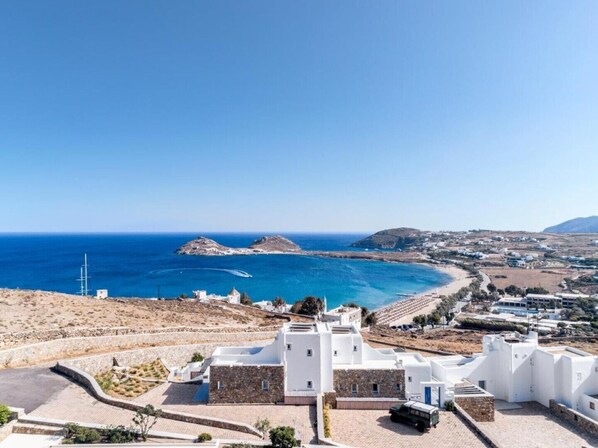 Vista costera con edificios blancos, mar azul cristalino y un paisaje montañoso en la distancia.