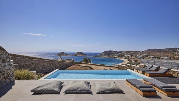 Una piscina con sillones de descanso y vistas al mar y las colinas.