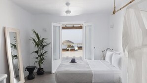 Un dormitorio minimalista con una cama, una planta en maceta, un espejo y vistas a la playa.