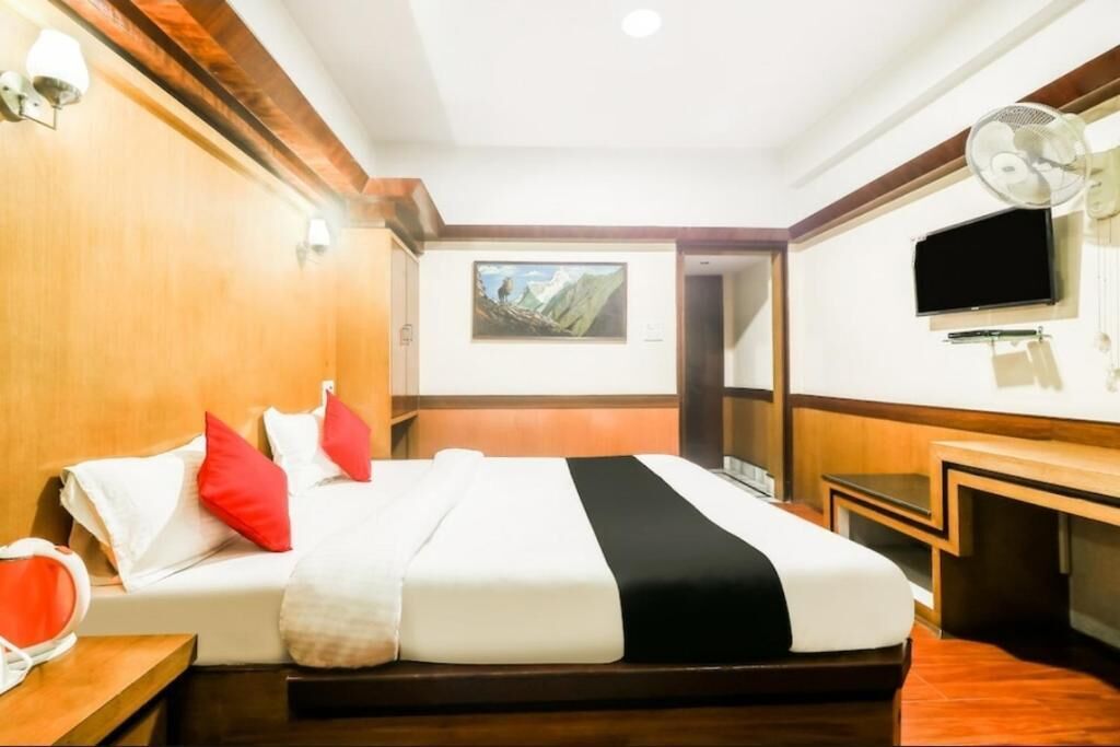 A hotel room with a bed, a TV, a desk, and a painting on the wall.