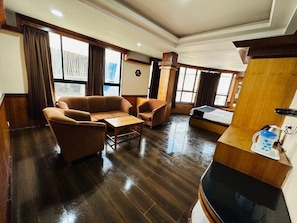 A spacious room with a wooden floor, a sofa, a small table, and a desk with a computer. - Hotel Gajraj (Gangtok)
