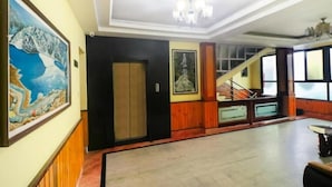 A spacious lobby with a staircase, a chandelier, and artwork on the walls. - Hotel Gajraj (Gangtok)