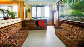 A reception area with a desk, two patterned sofas, a large painting of a forest, and a sign reading "CAPITAL O". - Hotel Gajraj (Gangtok)