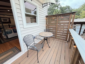 Une terrasse en bois avec une table et des chaises en métal, une fenêtre avec des stores et une clôture en bois.