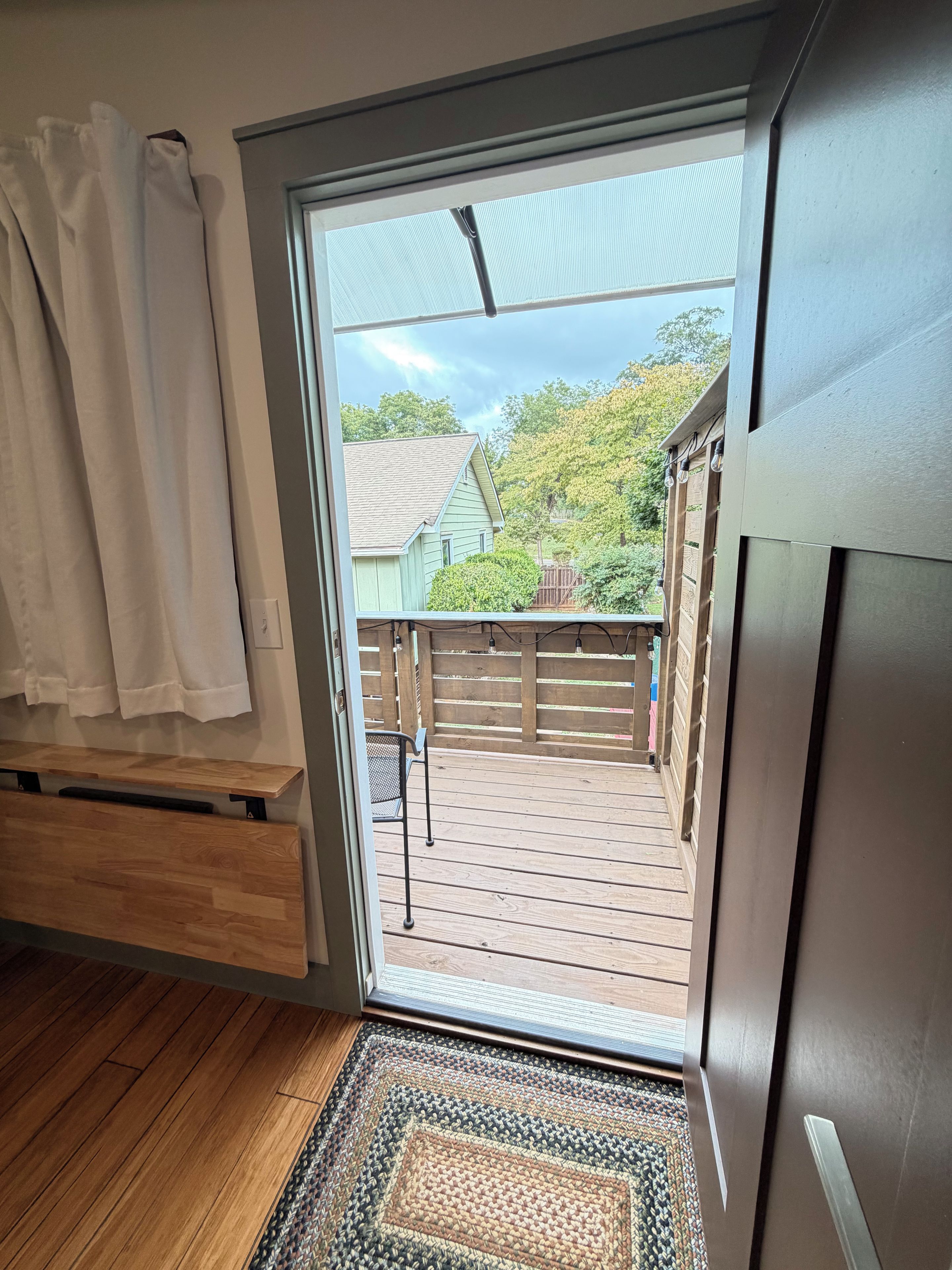 Eine Holzterrasse mit Blick auf ein Haus und Bäume, einem Metallstuhl und einer Holzbank.