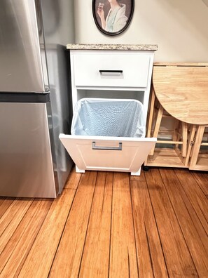 A kitchen with a stainless steel refrigerator, a white drawer unit, and a wooden dining table. - The Backyard Bungalow On The Trail -just minutes from downtown (Greenville)