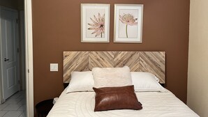 A bedroom with a wooden headboard, two framed floral pictures, a white bedspread, and a brown leather pillow. - Spacious, Comfortable Home Near Golf, Biking, Hiking & Restaurants (Tucson)