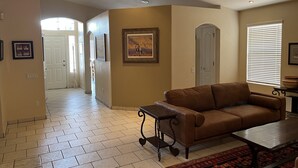 A living room with a brown sofa, a coffee table, and a patterned rug. There is a door and a window with blinds. - Spacious, Comfortable Home Near Golf, Biking, Hiking & Restaurants (Tucson)