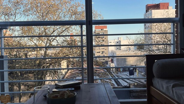 Ein Zimmer mit großem Fenster, einem Holztisch mit Schüssel und Tasse sowie einem Bett.