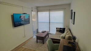 Ein modernes Wohnzimmer mit Flachbildfernseher, Couch, Holztisch und Schreibtisch mit Laptop.