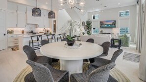 Eine moderne Küche mit weißen Schränken, ein Essbereich mit Korbstühlen und eine große Insel mit einem weißen Tisch.
