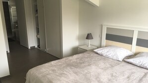 A bedroom with a bed, nightstand, and a lamp. There is a closet with sliding doors and a bathroom visible in the background. - Classified 4★ Landes house with swimming pool, in town center and beach nearby. (Messanges)