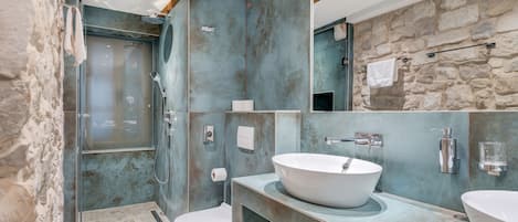 Un baño moderno con pared de piedra, un lavamanos grande de color blanco y mampara de ducha de vidrio.