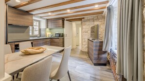 A modern kitchen with wooden beams, a stone accent wall, and a dining area with a table and chairs. - Mint Luxury Rooms (Split)