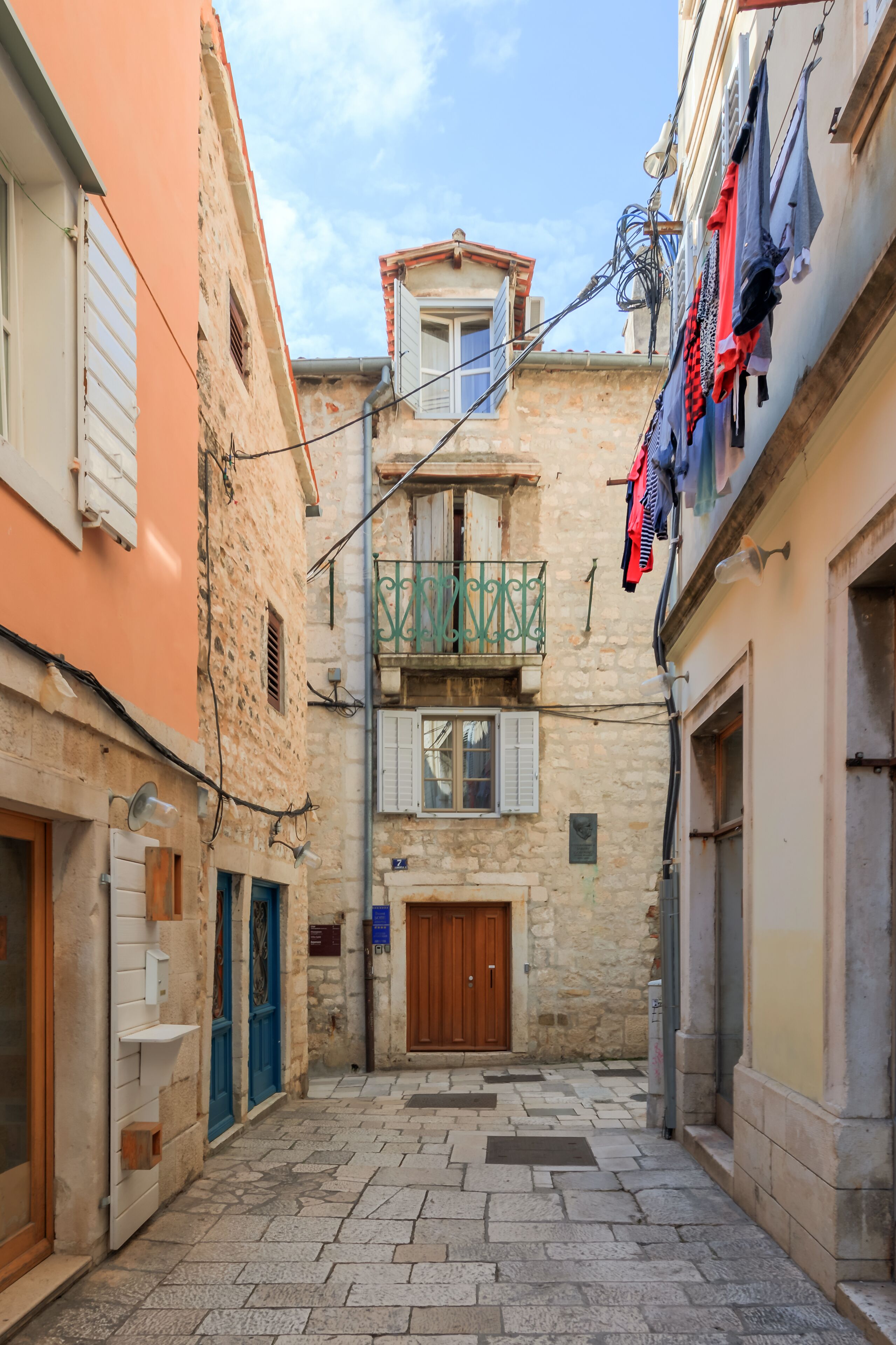 Una stretta via con edifici in pietra, una porta di legno e un balcone con panni stesi.