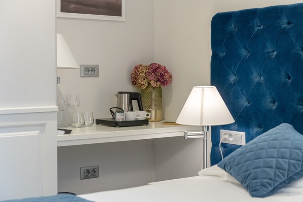 Quarto de hotel com cama, mesa de cabeceira, luminária, um vaso com flores e cafeteira.