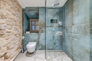 A modern bathroom with a stone wall, a glass-enclosed shower, a toilet, and a sink.