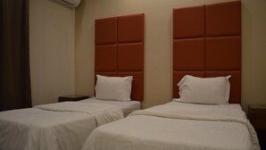 Dos camas individuales con cabeceras, ropa de cama blanca y una mesita de noche pequeña.