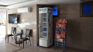 Un hall con zona de estar, dispensador de bebidas, televisor y estantería con revistas.