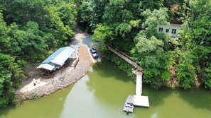 Une rivière avec un quai et un petit bateau. On aperçoit une zone abritée avec un véhicule et un bâtiment en arrière-plan.