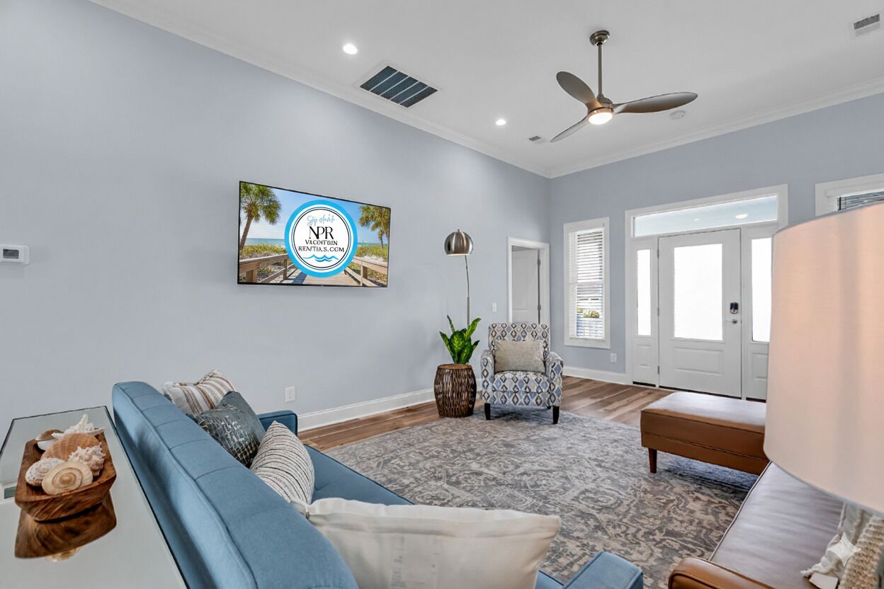 A living room with a blue sofa, a patterned rug, a ceiling fan, and a framed picture on the wall.