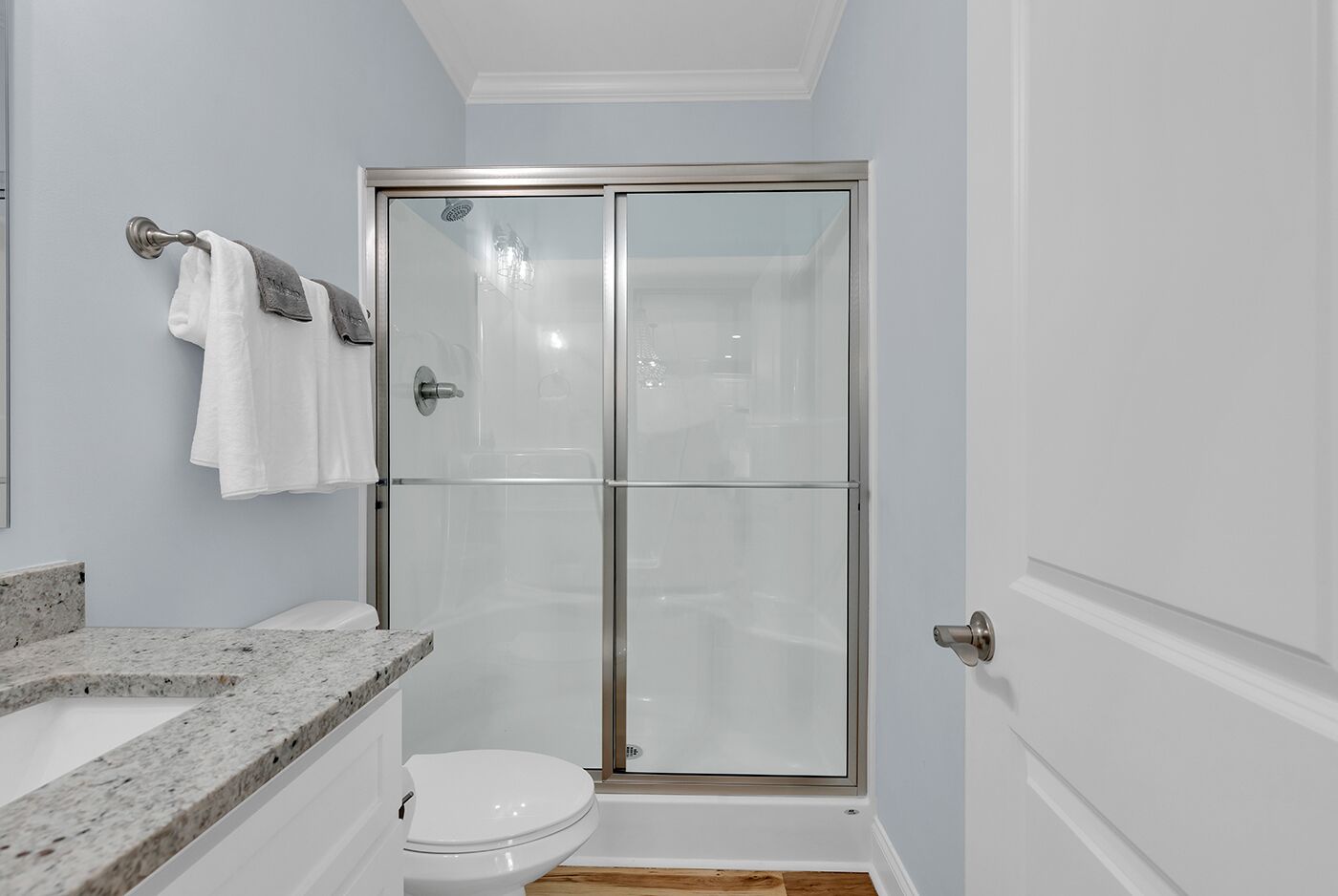 A bathroom with a glass shower enclosure, a marble countertop, and a white toilet.
