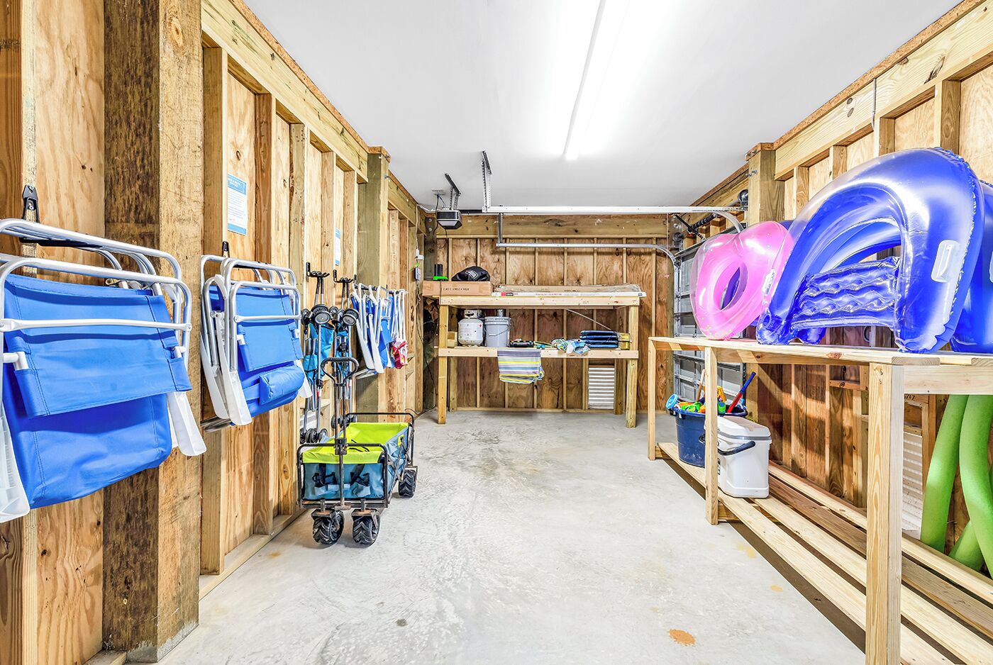 A wooden interior with a concrete floor, a cart with blue and green items, and shelves with inflatable rings and a helmet.