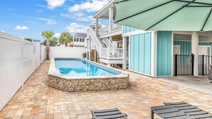 Ein Schwimmbecken mit Steinverkleidung, eine überdachte Terrasse und eine Treppe zu einer oberen Dachterrasse.