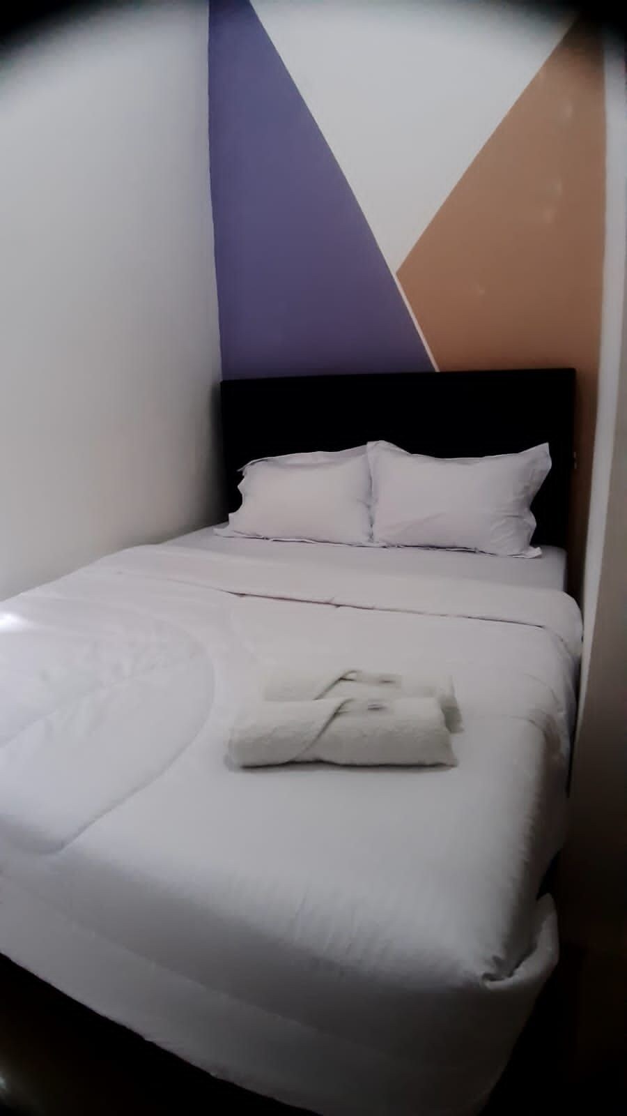 Una cama bien hecha con ropa blanca y una toalla doblada encima.