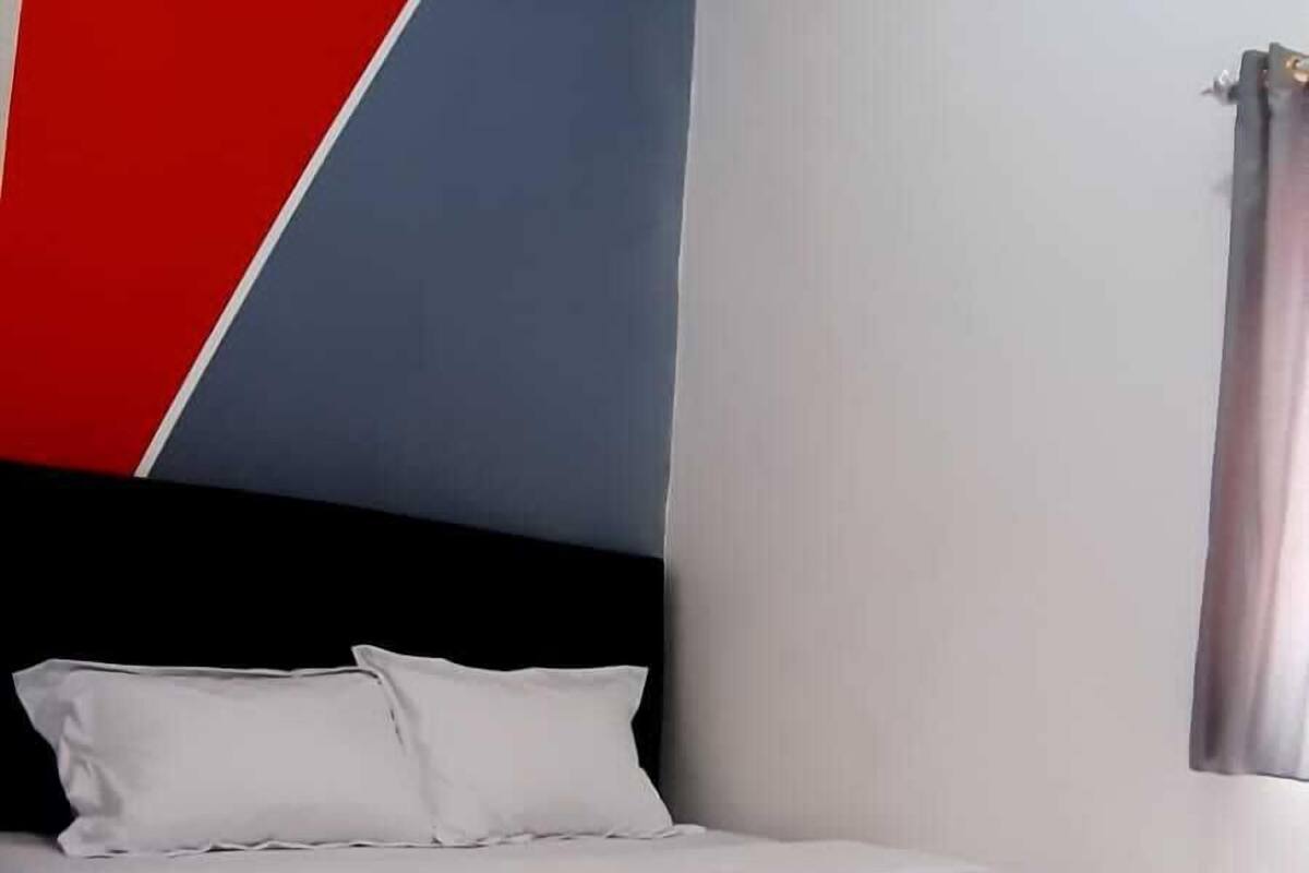 Ein ordentlich bezogenes Bett mit weißen Leinen in einem Raum mit geometrischem Wanddesign und einem Fenster mit Vorhängen.