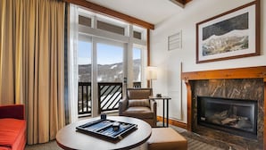 A cozy room with a fireplace, a table with a board game, a comfortable chair, and a view of the outdoors through large windows. - Adjoining Studios on Top floor @Spruce Peak! (Stowe)