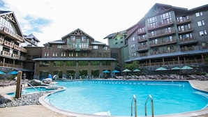 A hotel with a large pool, multiple balconies, and outdoor seating areas. - Adjoining Studios on Top floor @Spruce Peak! (Stowe)