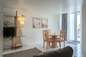 Ein Wohnzimmer mit einer Glasregal, einem Flachbildfernseher, einem Esstisch mit Stühlen und einem Sofa.