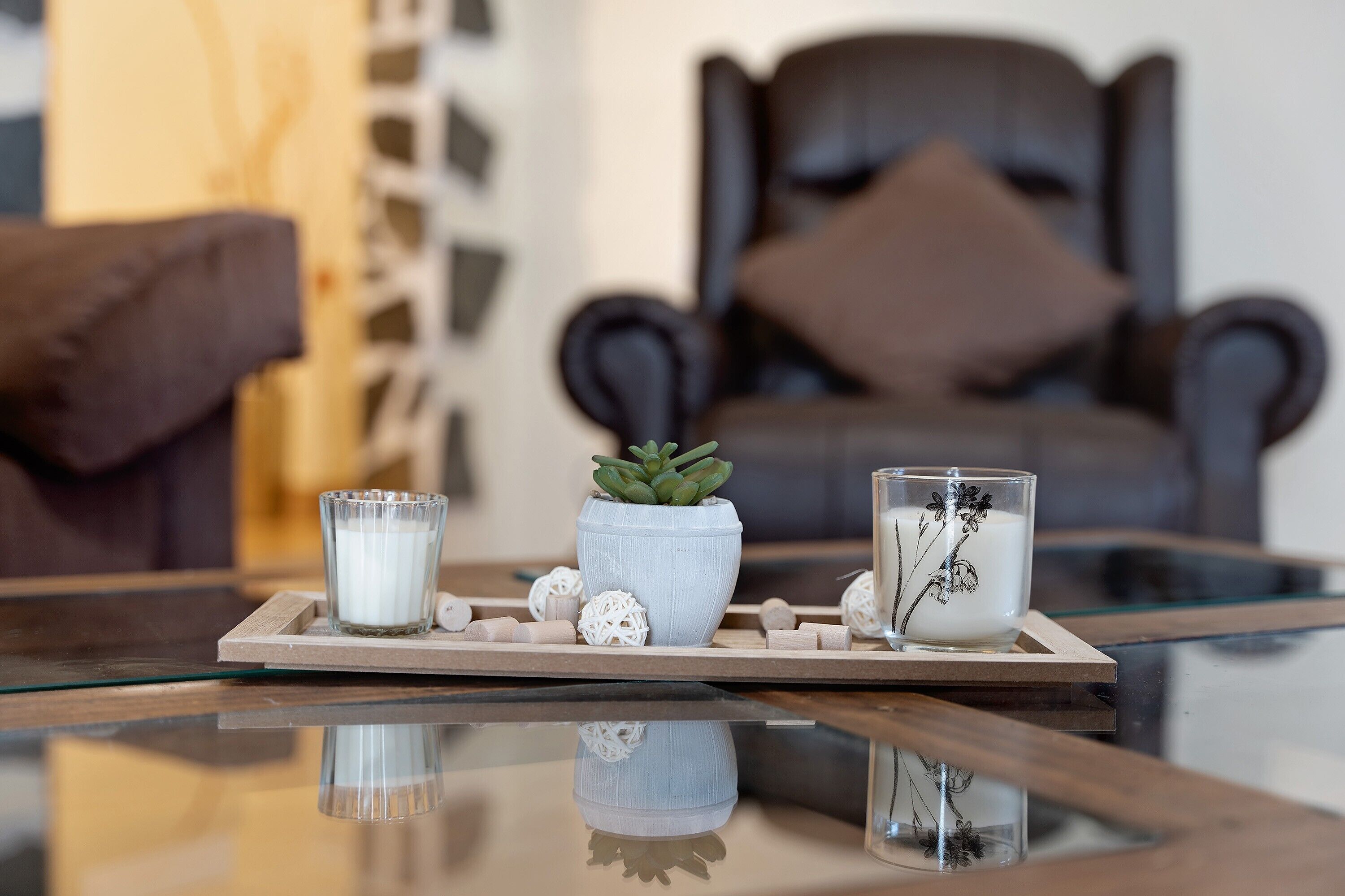 A modern living room with a glass coffee table, a potted succulent, decorative glassware, and a dark armchair with a cushion.