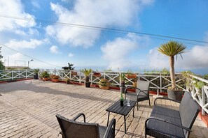 Une terrasse sur le toit agrémentée de plantes en pot, une table avec des chaises et une vue sur le ciel.