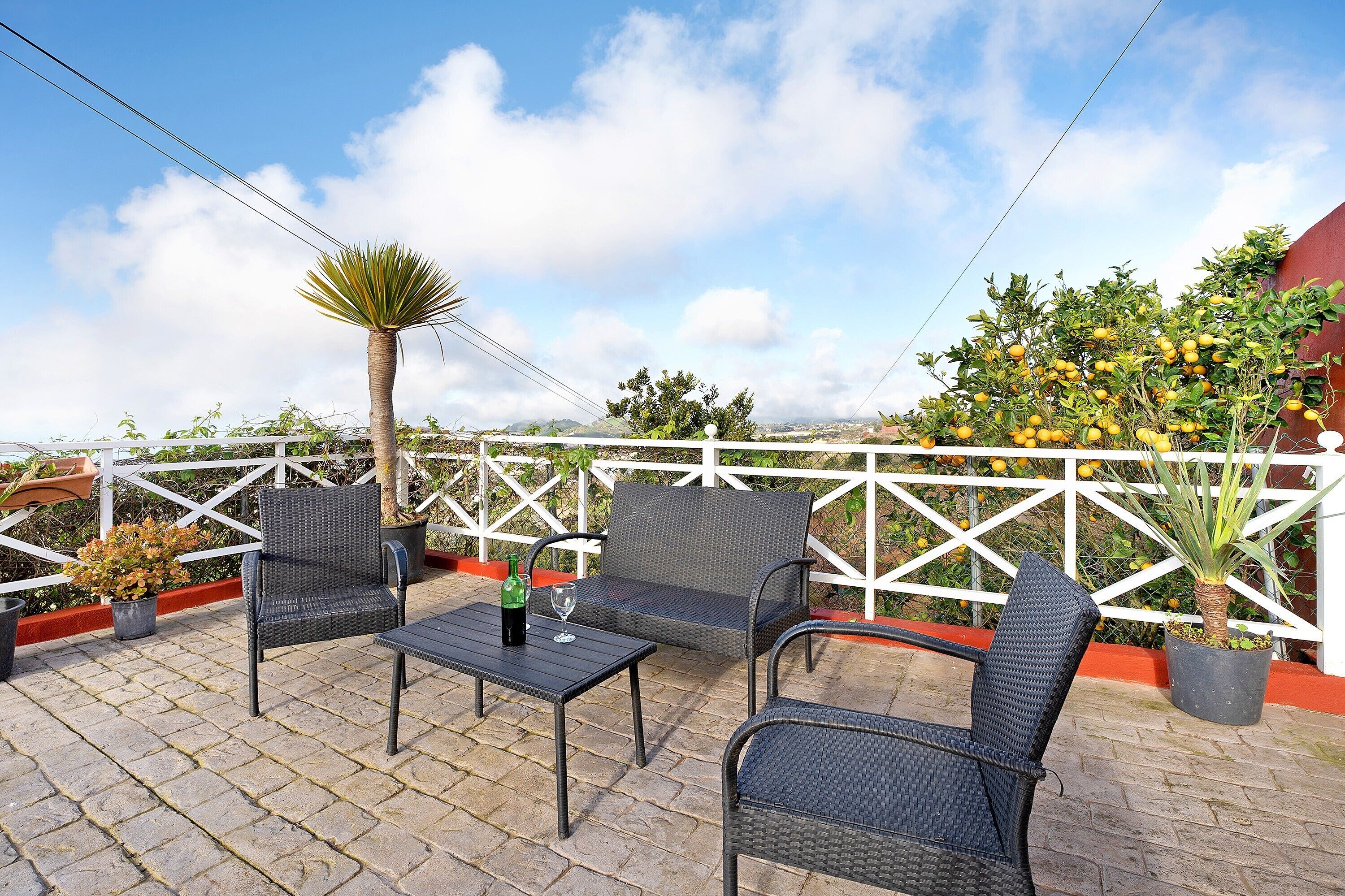 Een terras met rieten stoelen en een tafel, een bloempot en uitzicht op de lucht.