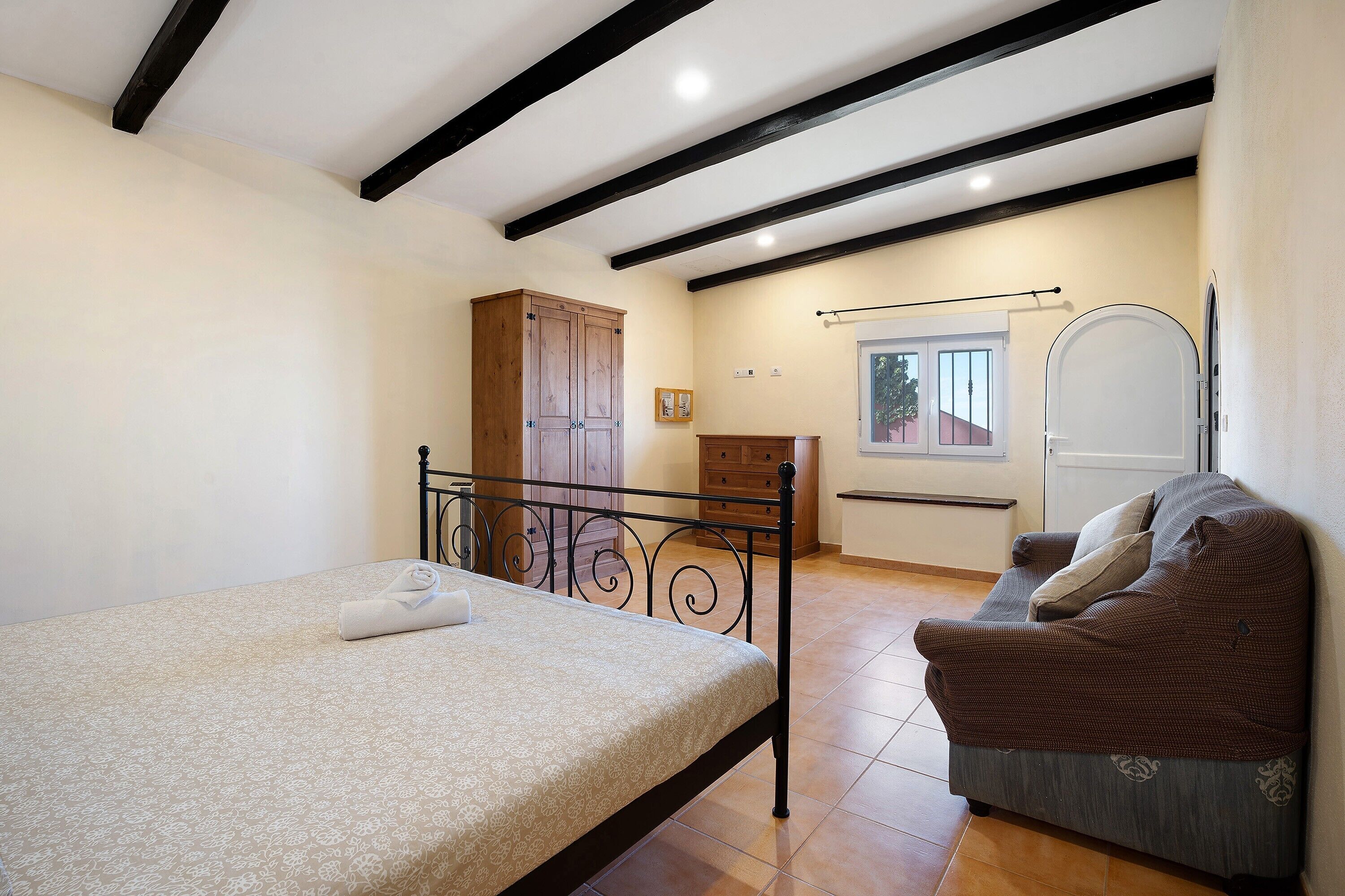 Een slaapkamer met een bed, een bank, een kledingkast en een raam.