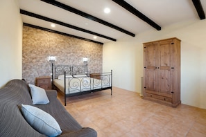 Un dormitorio con pared de piedra, una cama con cabecero metálico, un armario de madera y un sofá gris con cojines.