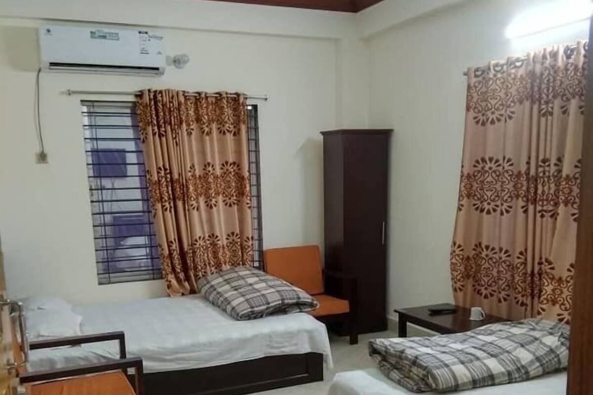 A bedroom with two beds, a wardrobe, an air conditioning unit, and a window with patterned curtains.