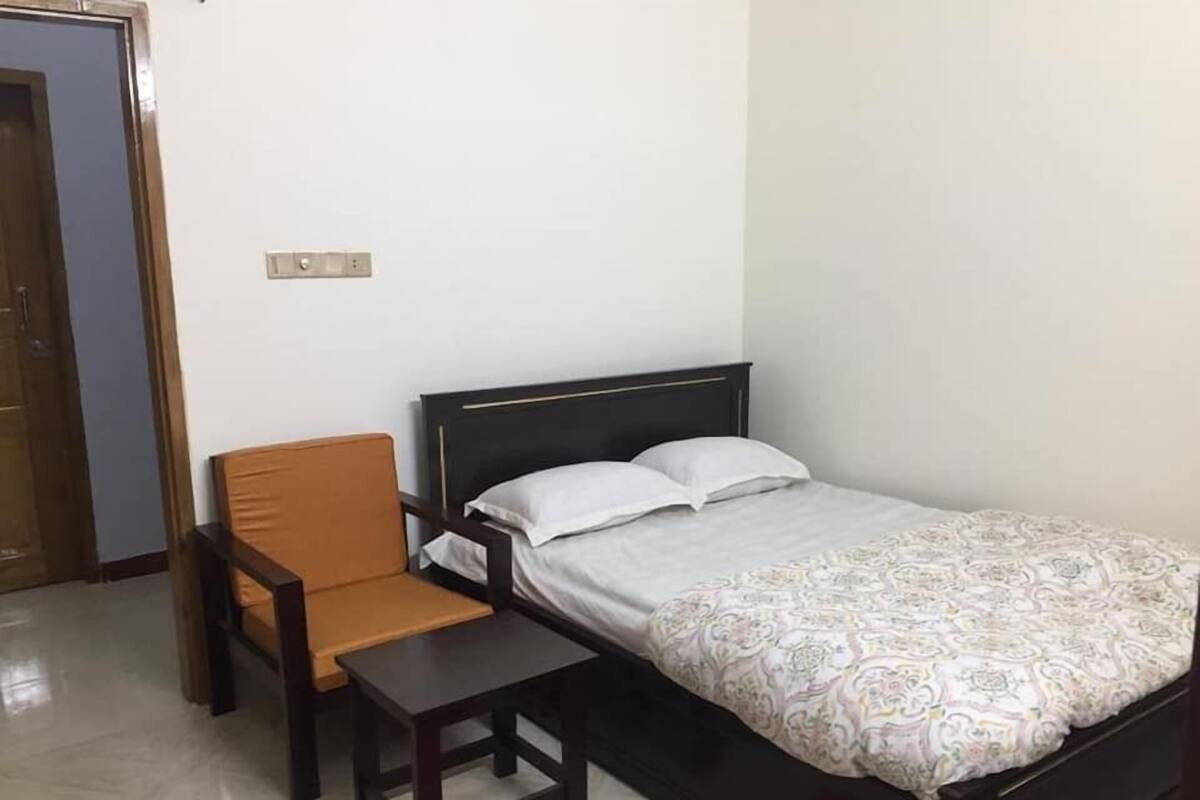 A small, neatly arranged bedroom with a single bed, a chair, and a small table.