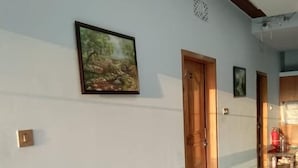 Un pasillo con una puerta de madera, un cuadro en la pared y un extintor rojo a lo lejos.