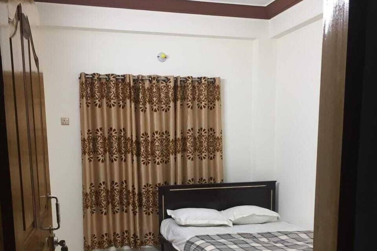 A bedroom with a bed, curtains, a ceiling fan, and a wooden door.