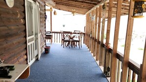 Un espace extérieur abrité, doté d’une moquette bleue, de tables et de chaises en bois, et d’un ventilateur de plafond.