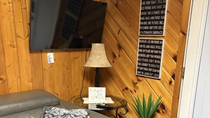Un salon moderne avec un canapé en cuir, un téléviseur fixé à un mur en bois, une lampe, une petite table avec une télécommande et une plante en pot.