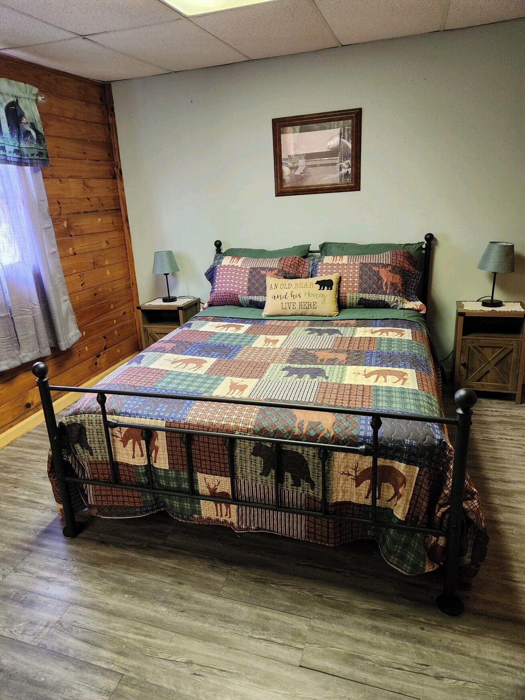Ein Bett mit einer Quiltdecke mit Tiermotiven, zwei Nachttischlampen, ein gerahmtes Bild an der Wand und Holzpaneele.